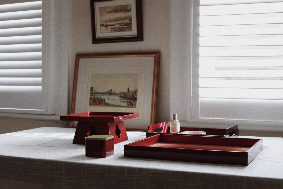 Vinidec red lacquered tray and box collection featured with raised pedestal table stand and small square box on a linen tablecloth