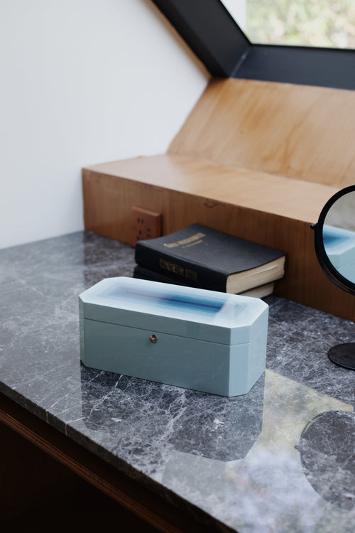Vinidec Chiaroscuro octagonal jewellery and watch box in baby blue gradient lacquer, styled on a dark marble vanity table