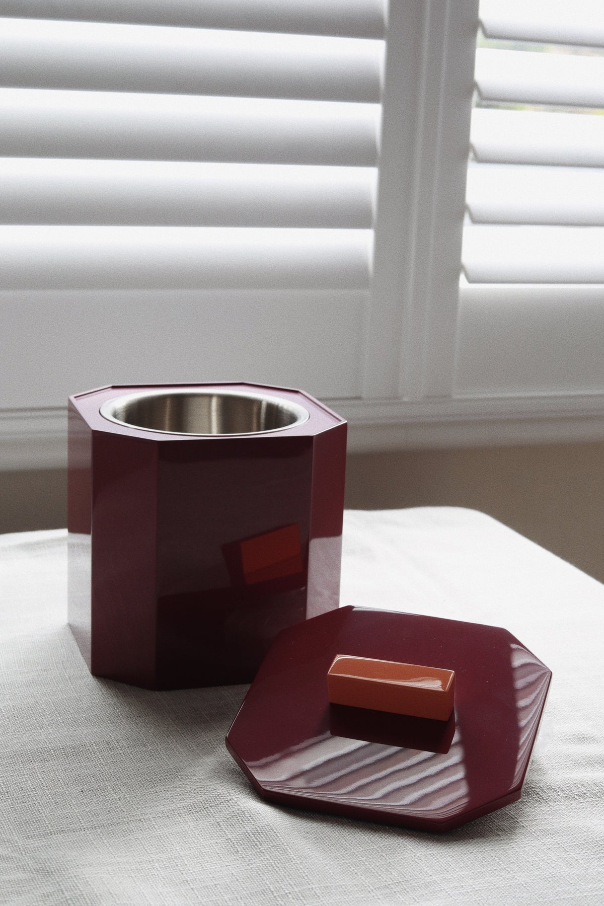 Vinidec high-gloss burgundy wine lacquer ice bucket shown open with double-wall stainless steel interior liner resting on a linen table for luxury holiday hosting setups.