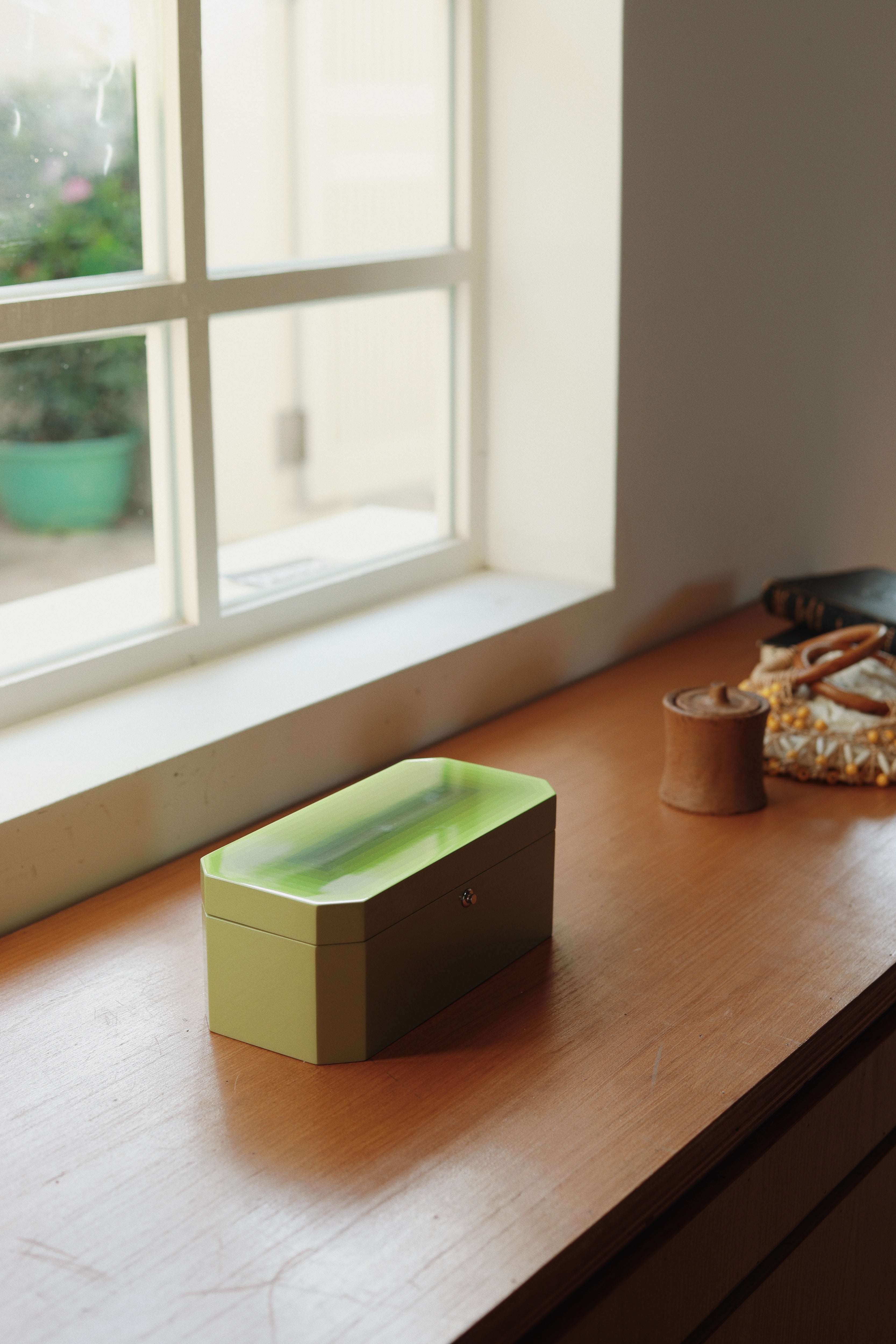 Vinidec Chiaroscuro octagonal jewellery and watch box in pistachio green gradient lacquer, styled on a wooden window sill