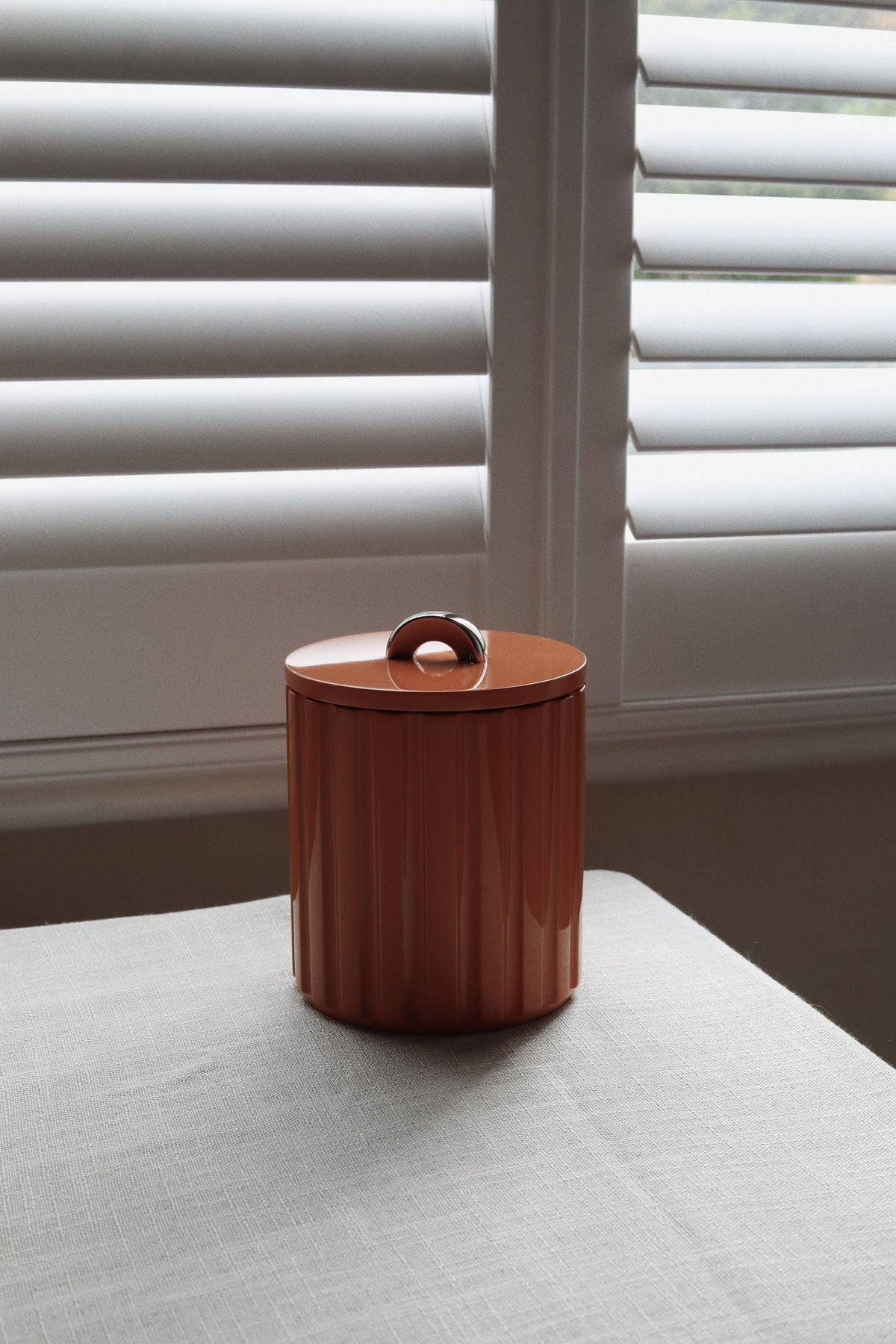 Vinidec fluted lacquer ice bucket in warm burnt amber with a polished chrome arc handle, set against a window with neutral linen for autumn tablescape styling.