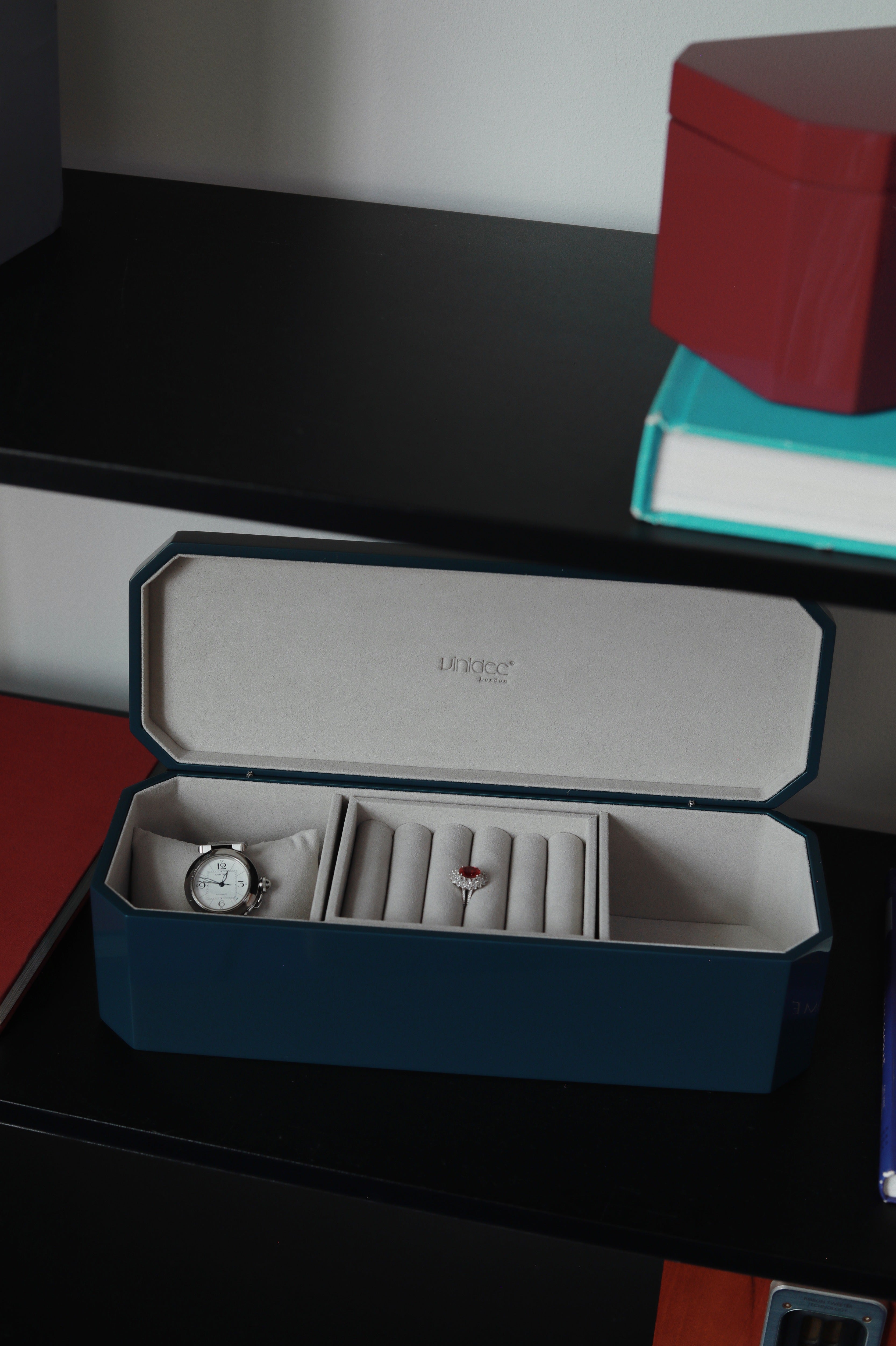 Vinidec octagonal jewellery and watch box in open dark blue lacquer, displaying a watch cushion and ring rolls on dark shelving