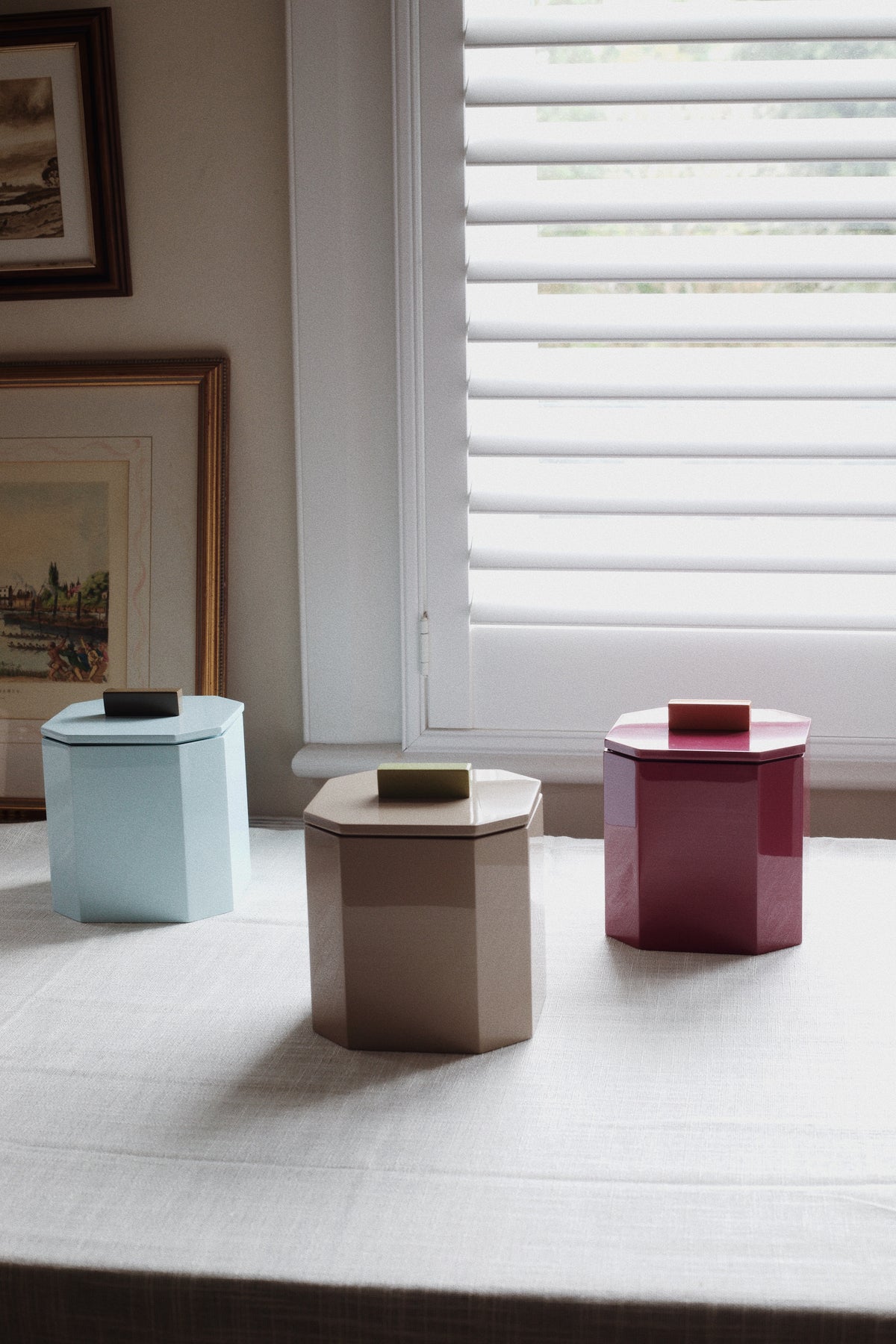 Trio of Vinidec octagonal lacquer ice buckets in powder blue, warm nude, and deep plum arranged on a dining table with framed art for fall dinner party tablescape styling. For bar cart decorating.