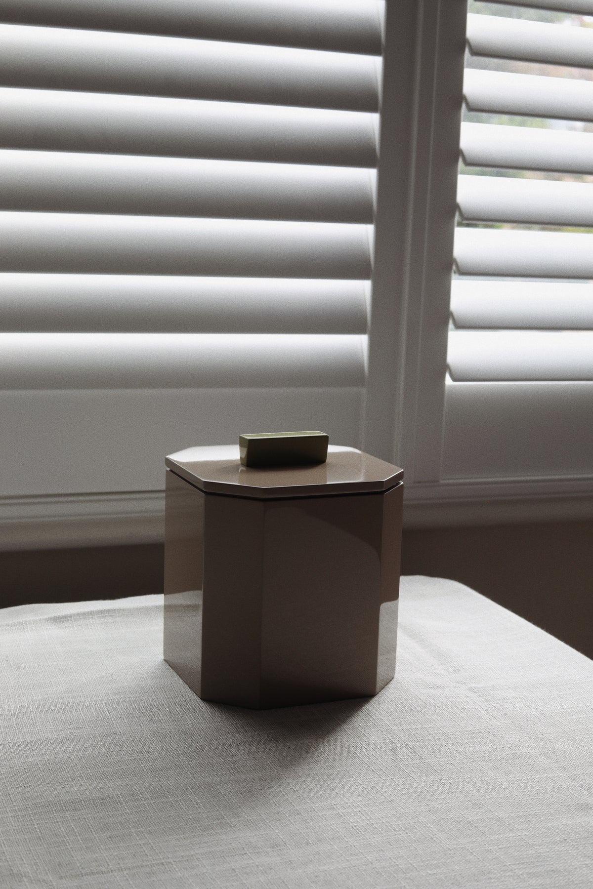 Vinidec octagonal taupe lacquer ice bucket with olive green contrast block handle styled on a linen dining table next to plantation window shutters for minimalist home bar ideas. 
