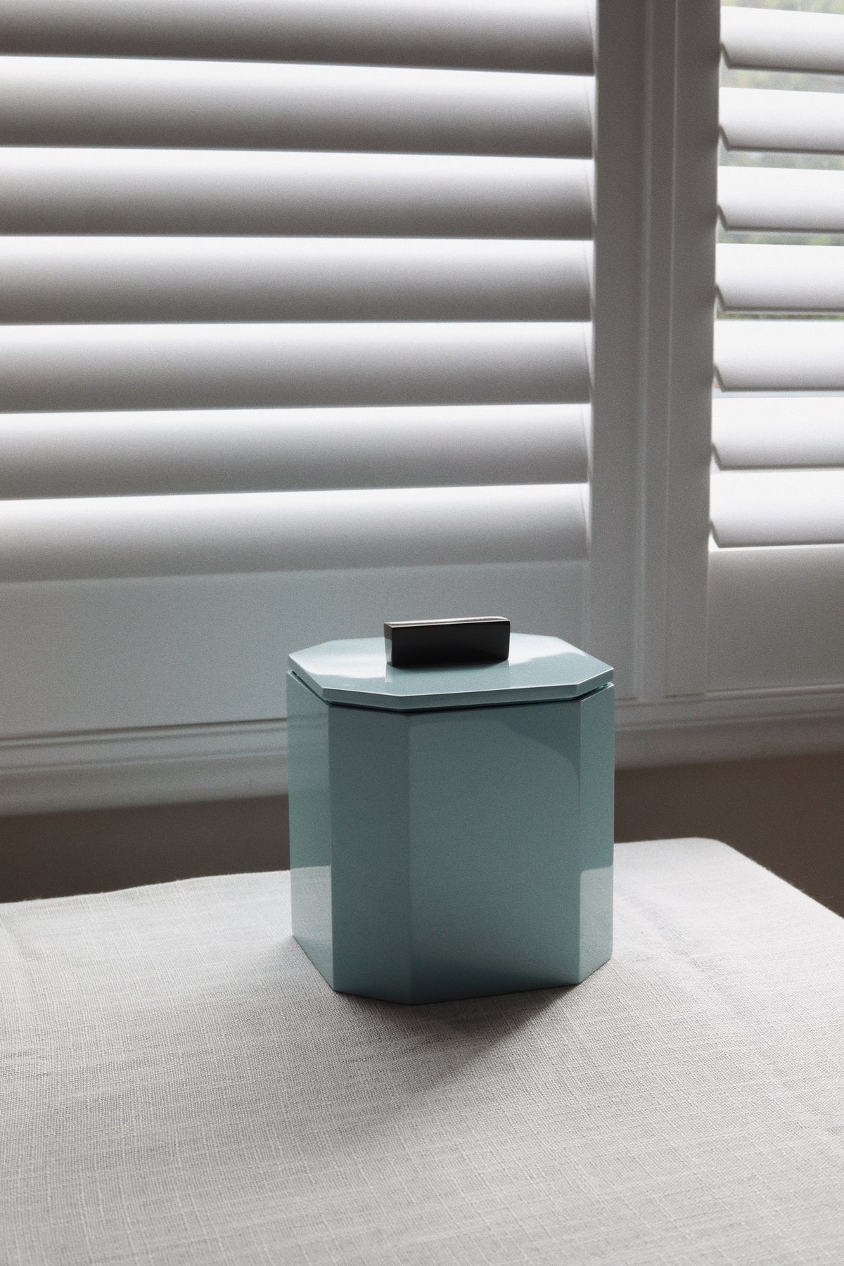 Vinidec geometric powder blue lacquer ice bucket with lid off showing insulated interior on white tablecloth for modern apartment bar cart accessories.
