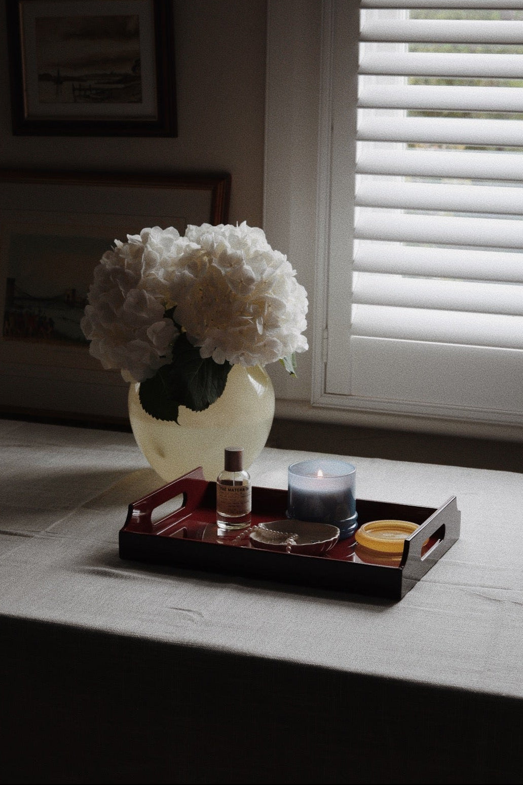 Vinidec dark red lacquered serving tray with handles holding candle and perfume beside white hydrangeas